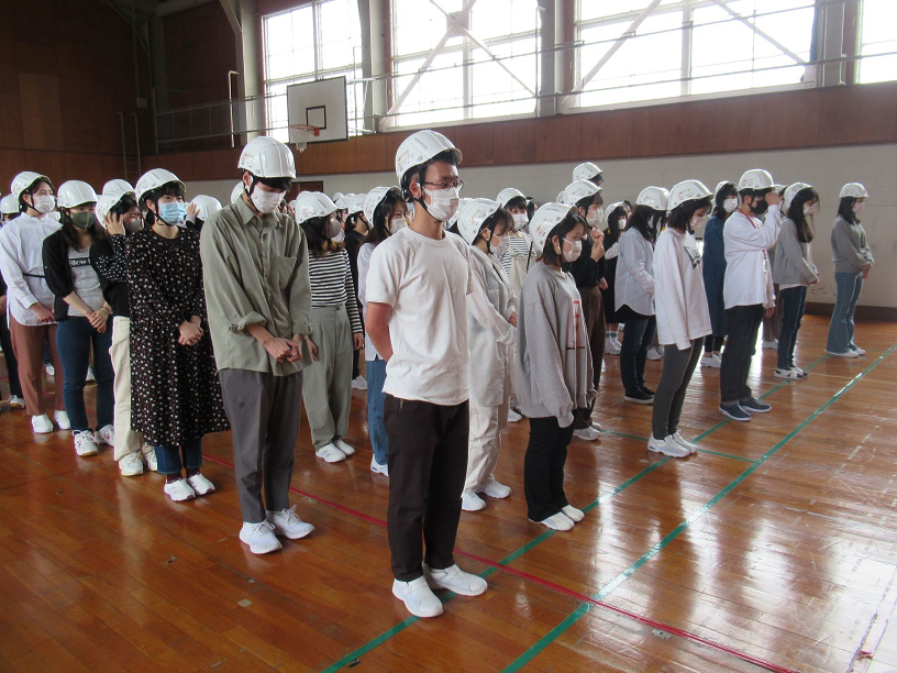 学生がヘルメットをかぶって体育館に集合しているところです。