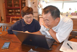 パソコンを操作する諸家さんと妻則子さんの写真