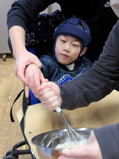 泡立て器で生地を混ぜる児童と職員