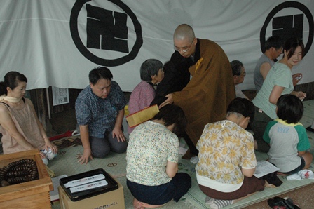 僧侶が教典で祭礼参加者の肩をたたく様子の写真